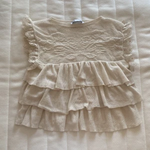 Beige volangtopp från Zara - Supersöt beige topp från Zara med broderade blommor upptill och spetsdetaljer på ärmarna. Toppen har flera lager volanger och är tillverkad i mjukt, ribbat material. Perfekt för dig som gillar romantisk och feminin stil. Står storlek m men den e liten i storleken så den passar xs och s (jag brukar ha s). Kontakta mig vid frågor🥰💞