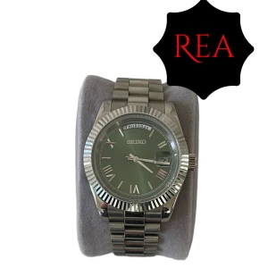 Oliv-Grön Seiko Mod Day-Date(Valfritt armband på köpet) - Stilren Seiko klocka med oliv-grön urtavla, romerska siffror och dag/datumvisning. Inspererad av Day-Date. Boetten och länken är i blankt silverfärgat stål och urtavlan har en snygg solreflex. Perfekt accessoar för dig som vill sticka ut med en klassisk men modern look. Alla länkar + box tillkommer självklart vid köp‼️🙌 
