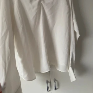 Vit blus från H&M i storlek 36 - Säljer en stilren vit blus från H&M i storlek 36. Blusen har långärmade ärmar och är gjord i ett tunt, flowy material som känns lätt och luftigt. Perfekt att styla med jeans eller kjol för en clean look.