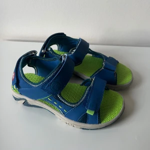 Blåa sandaler från PAX med grön sula - Snygga blå sandaler från PAX med justerbara kardborreband och grön mönstrad innersula. Skorna har robust yttersula i blått och grått. Innermått ca 19-20cm.