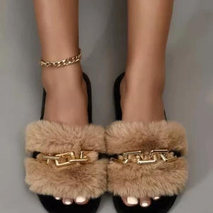 Svarta sandaler med beige fuskpäls - Snygga svarta sandaler med fluffig beige fuskpäls och chunky guldfärgad kedjedetalj över foten. Platt sula och öppen tå gör dem perfekta för chill dagar. Riktigt trendiga och sköna att glida runt i, passar till både jeans och shorts.