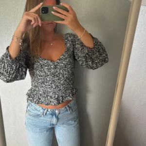 Blommig svartvit blus från Bik Bok - Supersöt blommig blus från Bik Bok i svart och vitt. Modellen har v-ringning, långa puffärmar och volangkant nertill. Tunn och luftig, perfekt till jeans eller kjol🥰