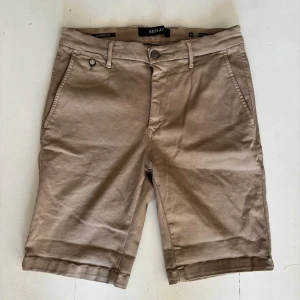 Beige shorts från Replay, storlek 31 - Snygga beige shorts från Replay i klassisk chino-stil. De har normal passform, bälteshällor, knapp- och dragkedjestängning samt fickor både fram och bak. Perfekta för varma dagar och enkla att matcha med det mesta.