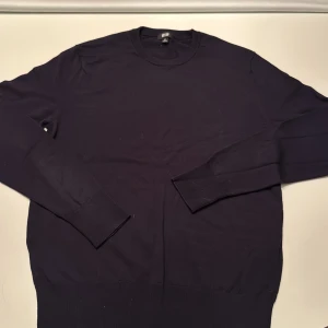 Mörkblå stickad tröja från Uniqlo XS - En stilren mörkblå stickad tröja från Uniqlo i storlek XS. Tröjan har rund halsringning, långa ärmar och ribbade muddar vid ärmslut och nederkant. Perfekt för lager-på-lager och enkel att matcha med olika outfits.
