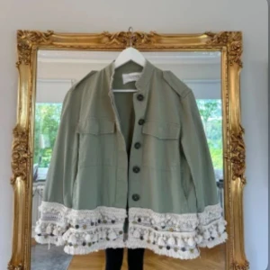 Grön overshirt med virkade detaljer - Ljusgrön overshirt med unika virkade detaljer och tofsar i beige. Så trendig och eftertraktad och säljs inte längre i butik! Funkar perfekt för allting, i helt nyskick bara testad