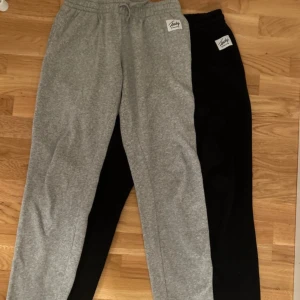 2-pack mjukisbyxor grå & svarta Rocky - Två par mjukisbyxor från Rocky, ett par i grått och ett i svart. Båda har elastisk midja med snörning och en liten vit logolapp framtill. Perfekta för chill eller träning, tillverkade i mjukt bomullsmaterial.