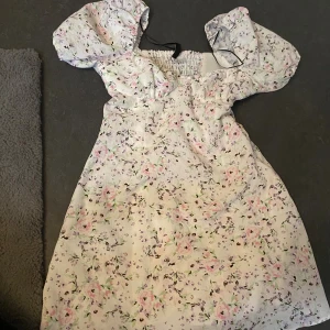 Blommig kortklänning med puffärmar - Supersöt kortklänning från H&M med blommigt mönster i pastellfärger. Klänningen har puffiga korta ärmar, smockad rygg och dragkedja i sidan. Perfekt för sommarens alla tillfällen och ger en romantisk vibe.