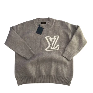 Grå stickad tröja från Louis Vuitton - Grå stickad tröja från Louis Vuitton med stort vitt LV-logo framtill. Tröjan har rund halsringning, ribbade muddar och en avslappnad passform. Perfekt för dig som vill ha en lyxig och stilren look med exklusiv känsla. Har ej riktigt bestämt priset än så kom med prisförslag!