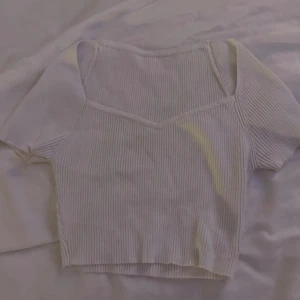 Vit ribbad croppad topp - Säljer en vit ribbad topp med v-ringning och korta ärmar. Toppen är croppad och har en snygg, figurnära passform som passar perfekt till jeans eller kjol. Materialet är mjukt och stretchigt för extra komfort.