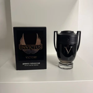 Paco Rabanne Invictus Victory EdP - En lyxig parfym i svart troféformad flaska med silverdetaljer och ett stort V på framsidan. Kommer i en elegant svart kartong med guldiga vingar och text. Doften är intensiv och maskulin, perfekt för dig som vill sticka ut.