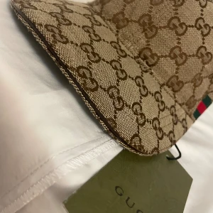 Gucci keps med GG-mönster - Byte funkar Snygg keps från Gucci i beige och brunt med klassiskt GG-monogram över hela kepsen. Justerbar rem baktill i brunt skinn och ikoniska gröna och röda ränder på sidan. Tillverkad i bomullscanvas med exklusiv känsla. Perfekt för dig som vill sticka ut med en lyxig accessoar.