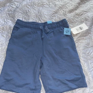 Blå shorts med snörning, strl 134/140 - Blå mjuka shorts med elastisk midja och snörning framtill. Klassisk rak passform och tillverkade i bomull, perfekta för chill dagar eller häng med kompisar. Fickor på sidorna för mobilen eller nycklar. Enkel stil som funkar till det mesta. Passar 11-13 år 