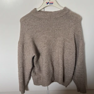 Beige stickad tröja från 157 - Mysig beige stickad tröja från 157 i storlek M. Tröjan har en avslappnad passform, ribbad halsringning och långa ärmar. Perfekt för lager-på-lager och chill dagar. Enkel att matcha med jeans eller kjol.