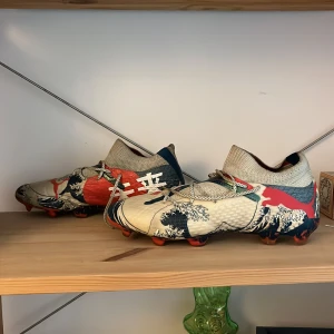 Puma fotbollsskor med våg-mönster, limited edition, elites. - Unika fotbollsskor från Puma med högt skaft och snörning. Skorna är inspirerade av en våg i Japan, limited edition. Snygga och stil rena går med vilket kit som helst. Skorna är puma så de är lite tunga men jag märkte inget av det efter ett tag.