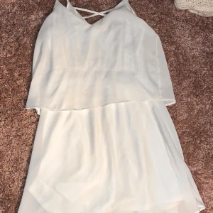 Vit kortklänning från Vila - Superfin vit kortklänning från Vila med tunna axelband och snygg v-ringning med korsade band framtill. Klänningen har ett luftigt lager på lager-utseende och är gjord i ett lätt, flowy material som känns som polyester. Perfekt för sommarens alla tillfällen!