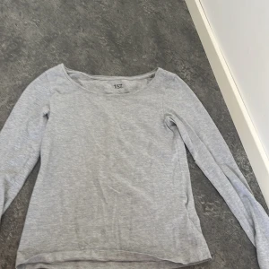 Ljusgrå långärmad tröja från 157 - En basic ljusgrå långärmad tröja från 157 med rund halsringning. Tillverkad i mjuk bomull, perfekt för lager-på-lager eller chill dagar. Enkel och stilren design som funkar till det mesta. tyvärr har tiden fått ett litet hål på vänstra armen, men går att sy hålet syns knappt. För liten för mig