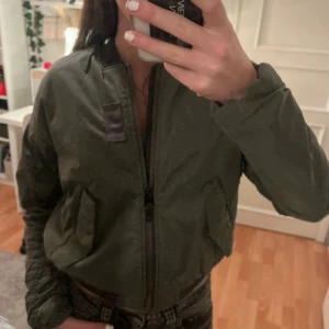 Olivgrön bomberjacka med dragkedja - Snygg olivgrön bomberjacka med klassisk passform och dragkedja framtill. Jackan har två fickor och ribbade muddar vid ärmslut och midja. Perfekt för dig som vill ha en stilren och trendig look. Skriv för flera bilder så löser jag! 