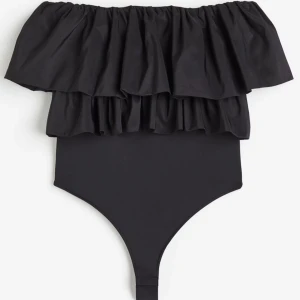 Svart body med volangdetalj - Supersnygg svart body med bred volang upptill som ger en trendig och feminin look. Off-shoulder design och enkel. Lappen är kvar.
