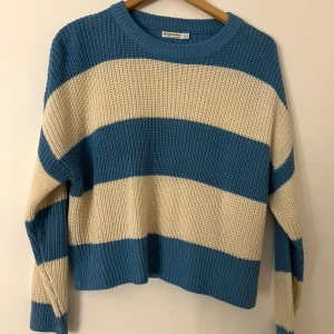 Randig stickad tröja från Stradivarius - Stickad tröja från Stradivarius med breda blå och beige ränder. Avslappnad passform, rund halsringning och långa ärmar. 
