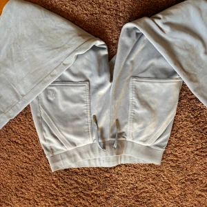 Ljusblåa mjukisbyxor från Juicy Couture - Snygga ljusblåa mjukisbyxor från Juicy Couture med bred resår och snörning i midjan. Byxorna har två stora fickor framtill och ett broderat JC-logo på ena fickan. Perfekta för chill eller häng med kompisar.