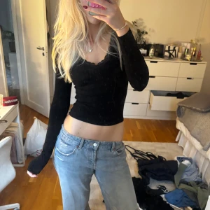 Svart croppad långärmad topp - Svart långärmad topp med croppad passform och v-ringad hals med spetskant. Sitter tight och har en enkel, stilren look som passar till mycket. Perfekt att matcha med jeans eller kjol för en snygg outfit.