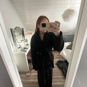 Svart kappa med bälte och stora slag - Säljer en svart kappa med bälte i midjan och stora slag. Perfekt för höst och vinter. Stängs med knappar framtill och har långa ärmar.