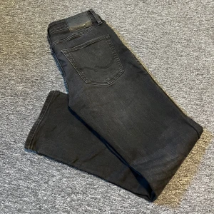 Svarta jeans från Jack & Jones - Svarta/mörkgråa jeans från jack&jones. Modellen heter Regular/Clark och är i storlek W29 L30. Dom är i hyfsat fint skick förutom att sömmen har lossnat lite vid högerfickan som man kan se på andra bilden annars fina jeans! Mvh 