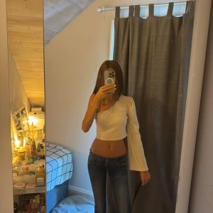 Beige one shoulder topp - Säljer en vit/beige topp med one shoulder-design och lång ärm. Den är vanlig i storleken och är lite stretchig. Den är aldrig använd men kommer tyvärr inte ihåg vart den är ifrån.