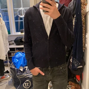 Mörkblå merinoull hoodie These Glory Days - Snygg mörkblå hoodie från These Glory Days i mjuk och lyxig merinoull. Tröjan har dragkedja framtill och långa ärmar. Perfekt för dig som gillar stilrena och bekväma plagg med premiumkänsla. Passar till jeans eller chinos.