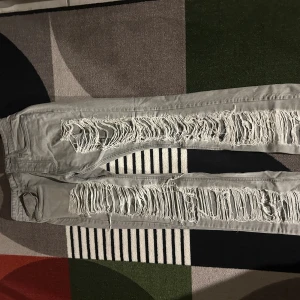 Grå ripped jeans från BoohooMAN - Säljer ett par grå jeans från BoohooMAN med extremt slitna och trasiga detaljer längs hela framsidan av benen. Byxorna har klassisk femficksdesign och smal passform. Perfekta för dig som gillar en edgy streetstil.