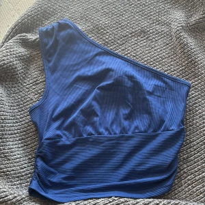 Blå oneshoulder topp från SHEIN - Säljer en blå ribbad oneshoulder topp från SHEIN i storlek S. Toppen har en tight passform och är tillverkad i ett stretchigt syntetmaterial. Perfekt för dig som vill ha en stilren och modern look med asymmetrisk axel.