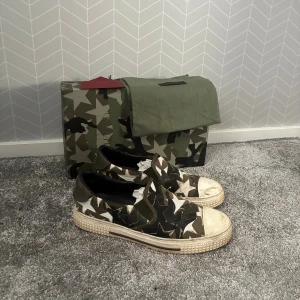 Valentino Garavani slip-on sneakers - Slip-on sneakers från Valentino Garavani med stjärnmönster i camouflagefärger. Skorna har en platt sula, rund tå och är tillverkade i skinn. Färgkombinationen är grön, beige, svart och vit. Kommer med originalkartong och dustbag.