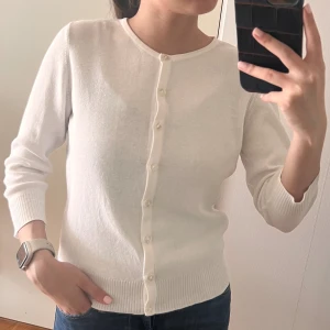 Vit kofta från Mexx med knappar - Snygg vit kofta från Mexx med rund hals och knäppning hela vägen fram. Tröjan har ribbade muddar och är perfekt för lager på lager. Långärmad och stilren design som funkar till jeans eller kjol.