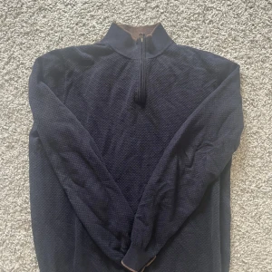 Mörkblå half zip-tröja Hansen & Jacob - Säljer en mörkblå långärmad tröja från Hansen & Jacob med brunt ribbstickat foder i kragen och half zip-dragkedja. Tröjan är i bomull och har en diskret struktur i tyget. Perfekt för dig som gillar stilren och klassisk look. Nypris är 1800 kr, mitt pris är 599 kr. Säljer då den inte används längre. Priset är ej hugget i sten.