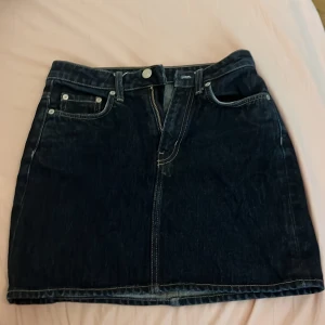 Mörkblå jeanskjol från WEEKDAY  - Säljer en snygg mörkblå jeanskjol från WEEKDAY med klassisk femficksdesign, bälteshällor och dragkedja framtill. Kjolen är kort och har kontrastsömmar som ger en cool vintagekänsla. Perfekt att matcha med sneakers eller boots.