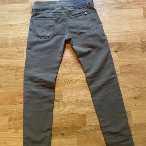 Grå slim från Jacob Cohen - Snygga grå byxor från Jacob Cohen med fin passform och klassiska fickor. Byxorna har en liten italiensk flagga vid bakfickan och ett mörkt Jacob cohen märke med logga i midjan. Tillverkade i mjuk bomull