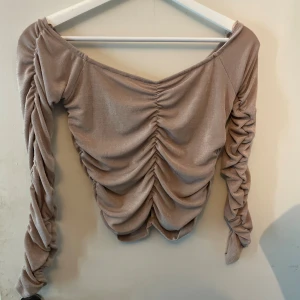 Beige omlottopp från Amisu - Trendig beige omlottopp från Amisu i storlek XL. Toppen har långa ärmar med snygg rynkdetalj och en croppad passform. Materialet är mjukt och stretchigt, perfekt för att skapa en cool och avslappnad look. Toppen sitter ganska tajt, jag som vanligtvis har S/M kunde använda den utan problem. Använd ett antal gånger! 