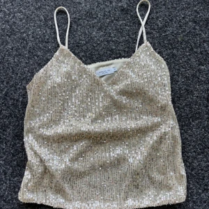 Glittrig guldig paljettopp Stockh LM - Supersnygg glittrig topp i guld med tunna axelband och v-ringning. Toppens yta är täckt av paljetter. Använt endast 2 gånger. Köpt för 680kr (pris kan diskuteras)