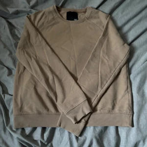 Beige sweatshirt från 157, storlek M - En basic beige sweatshirt från 157 i storlek M. Tröjan har rund halsringning, långa ärmar och ribbade muddar vid ärmslut och nederkant. Perfekt för en chill och avslappnad stil. Tillverkad i mjuk bomullsmix för extra komfort.