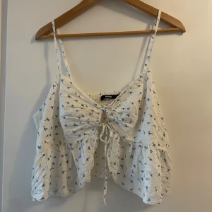 Gulligt linne med knytdetaljer  - Ett gulligt linne från bikbok med blåa blommor på. Den är öppen framtill och knyts på önskar sätt vid bysten. Banden är justerbara. Storlek XL men jag är en storlek M och den sitter bra på mig! Tack vare knytningen vid bysten framtill och justerbara band går den att anpassa utefter hur man vill att den ska sitta! 