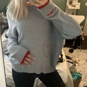 Ljusblå stickad tröja Zadig & Voltaire - Ljusblå stickad tröja från Zadig & Voltaire med röd broderad text 'AMOUR' på ärmslutet och ett rött hjärta broderat framtill. Tröjan har långa ärmar, ribbade muddar och röd detalj vid ärmslut. Oversized och riktigt mysig.