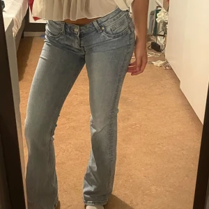 Lågmidjade jeans - Säljer ett par ljusblå jeans med bootcut-modell och klassisk femficksdesign. Jeansen har låg midja och är tillverkade i mjukt denimtyg som ger en avslappnad vibe. Perfekta för dig som gillar en retroinspirerad look med utsvängda ben.