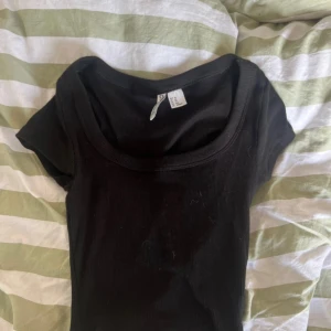 Svart ribbad topp från H&M Divided - Säljer en svart ribbad topp från H&M Divided i storlek XS. Toppen har rundad halsringning och korta ärmar, perfekt att styla med jeans eller kjol. Materialet är mjuk bomull och modellen är normal passform. Enkel och stilren design som funkar till många looks.