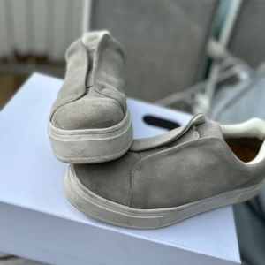 Eytys, strl 43 - Snygga grå sneakers i mocka från eytys med vit sula och diskret lila detalj baktill. Skorna har en minimalistisk design utan synlig snörning, vit insida och korkinnersula för extra komfort. Använda ca 10 gånger under sommaren, därav lite smutsiga men fortfarande i bra skick.