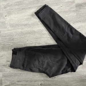Replay svarta slim jeans - Svarta jeans från Replay med diskret tvättad look och klassiska fem fickor. Byxorna har smal passform, svarta sömmar och Replay-logga på linningen. Perfekta för dig som gillar stilrena och moderna jeans med snygg detalj på bakfickan.