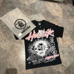 Svart Hellstar t-shirt med tryck - Svart t-shirt från Hellstar med stort grafiskt tryck framtill i vitt och rosa samt texten 'Hellstar Records' på ryggen. T-shirten har rund hals och korta ärmar. Materialet är mjuk bomull och passformen är normal. Perfekt för dig som gillar streetwear och unika prints.