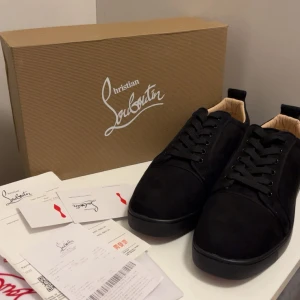 Christian Louboutins - Säljer ett par svarta sneakers från Christian Louboutin i mocka med klassisk röd signatursula. Skorna har rund tå, snörning och en stilren, minimalistisk look. Insidan är ljusbeige och de kommer med originalkartong och äkthetsbevis. Perfekta för dig som gillar lyxiga detaljer.