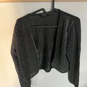 Glittrig svart bolero från KappAhl - Snygg svart glittrig bolero från KappAhl, Number One. Koftan har lång ärm. Använd endast en gång. Perfekt till fest och finare tillfällen. 