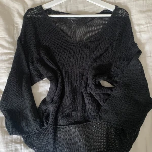 Svart stickad tröja från KappAhl - Svart stickad tröja från KappAhl i loose fit med v-ringning och lång ärm. Tröjan har ett grovmaskigt, luftigt stickat material som ger en avslappnad vibe. Perfekt att slänga över ett linne eller bikini under varmare dagar.