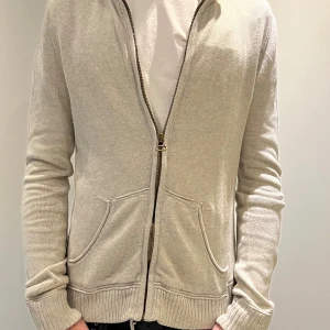 Beige kofta från Polo Jeans Company - Snygg beige kofta från Polo Jeans Company by Ralph Lauren. Tröjan har dragkedja framtill, två fickor och ribbade muddar. Tillverkad i mjuk bomull med en touch av kashmir för extra komfort. Perfekt för lager-på-lager och chill stil.